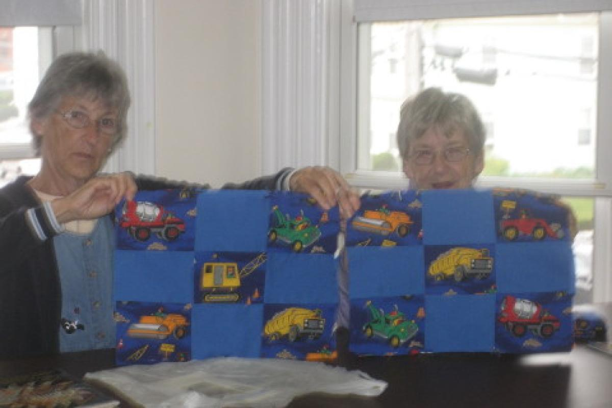Women Holding Blue Quilt with Vehicles